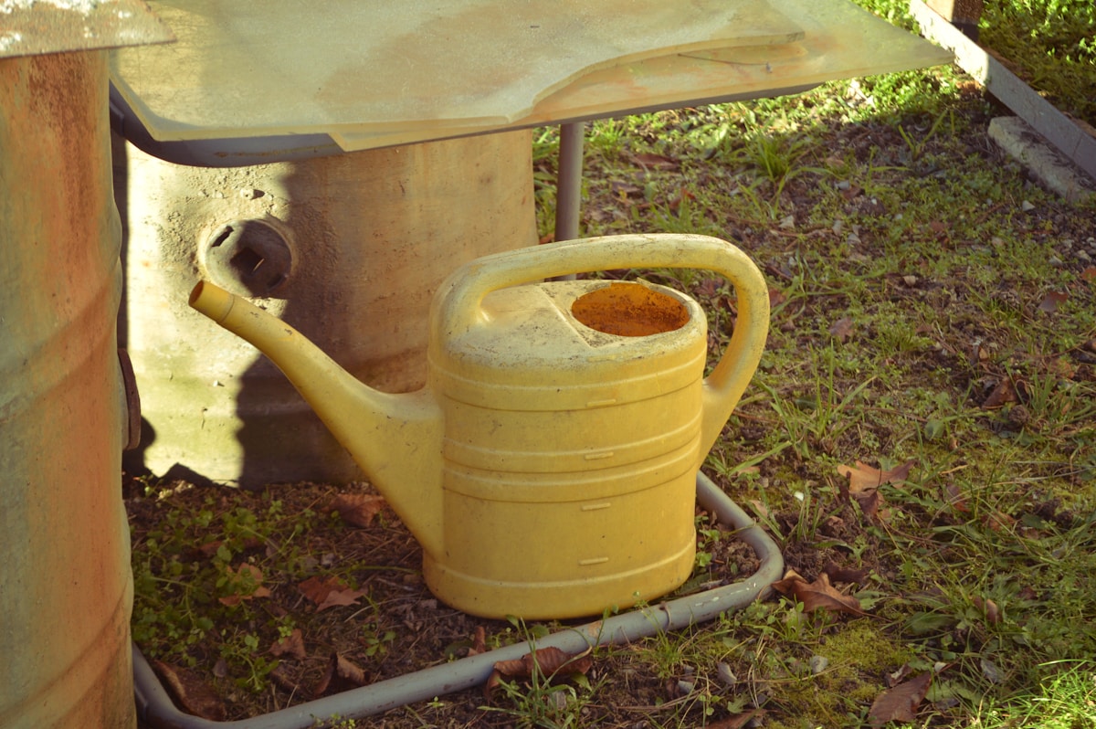 A yellow watering can sits on grass.