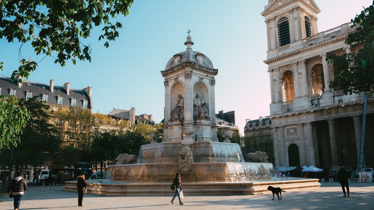 Fontaine ornementale dans une place publique parisienne avec bâtiments historiques.