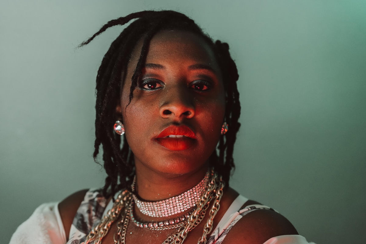 Femme noire avec des dreads, maquillage rouge vif, bijoux dorés.