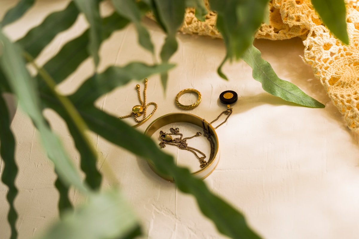 Bijoux dorés et feuillage vert sur fond texturé.