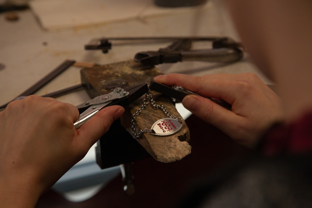 Outils de joaillerie, pince, pendentif en bois, chaîne métallique.