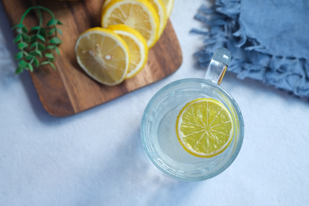 Verre d'eau avec tranche de citron, herbes fraîches et tranches de citron sur planche de bois.