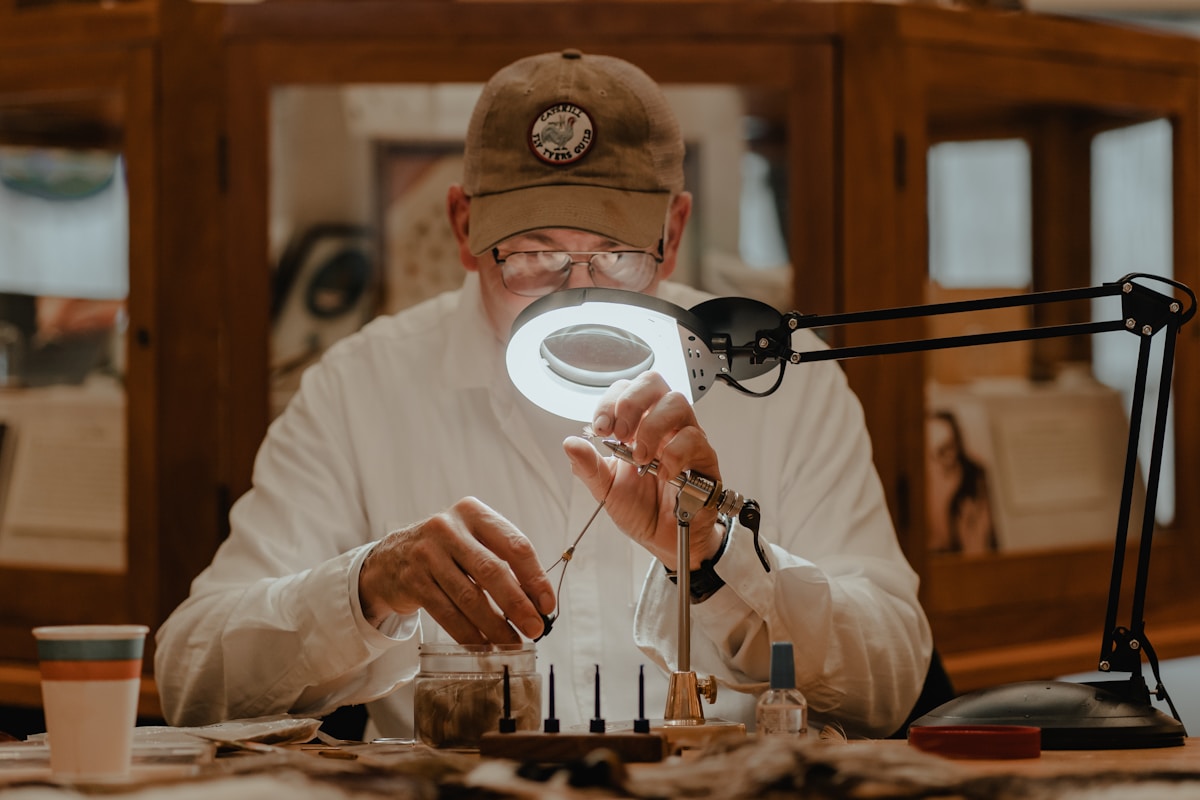 Homme en casquette examinant attentivement un objet sous une loupe.