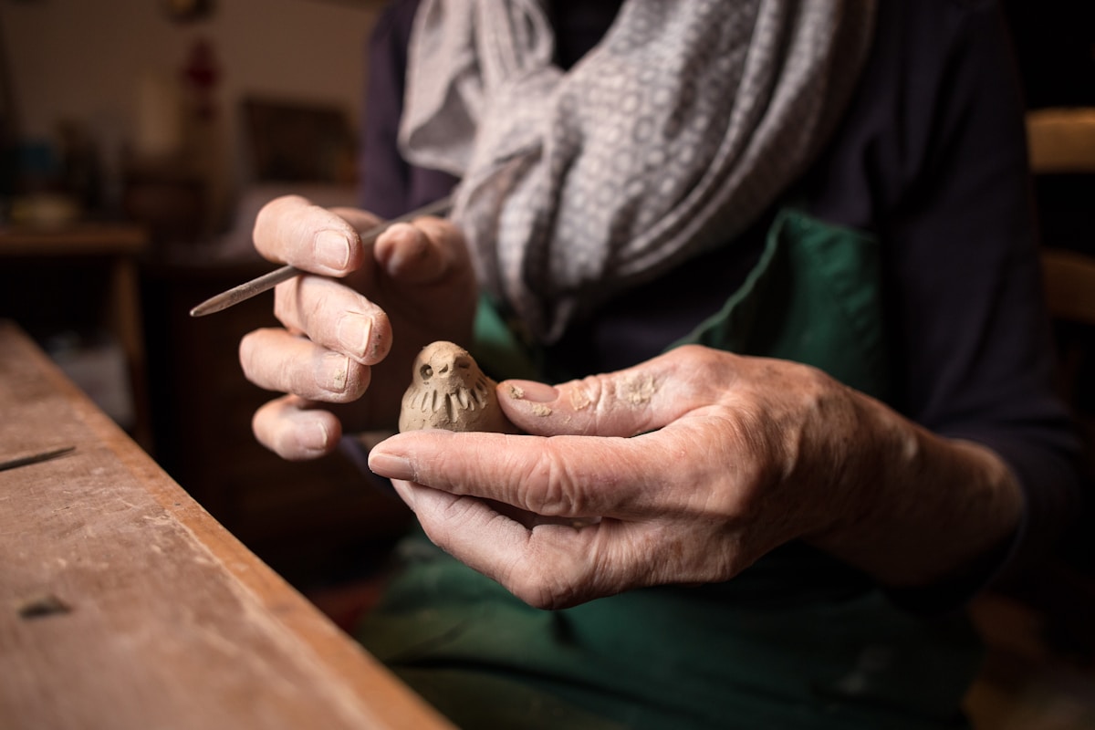 Mains âgées sculptant une figurine en argile sur une table en bois.