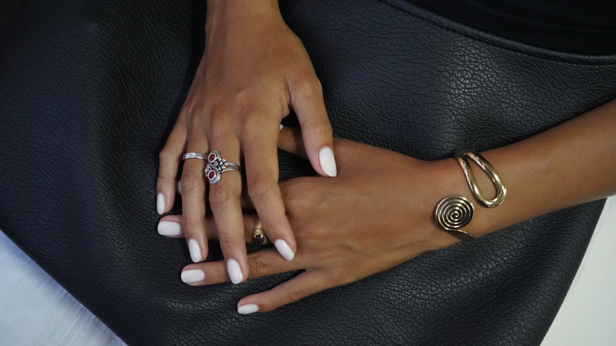 Mains féminines ornées de bijoux sur un siège en cuir noir.