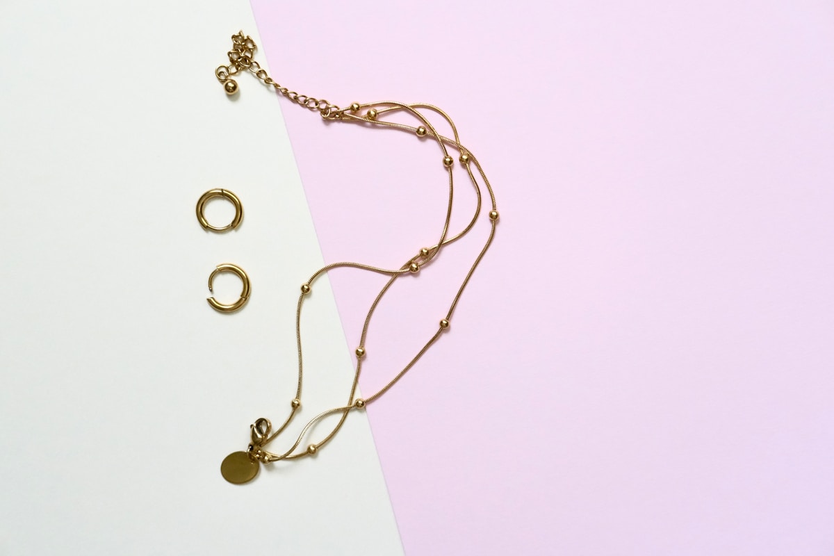 Collier en or avec pendentif et anneaux sur fond blanc et rose.