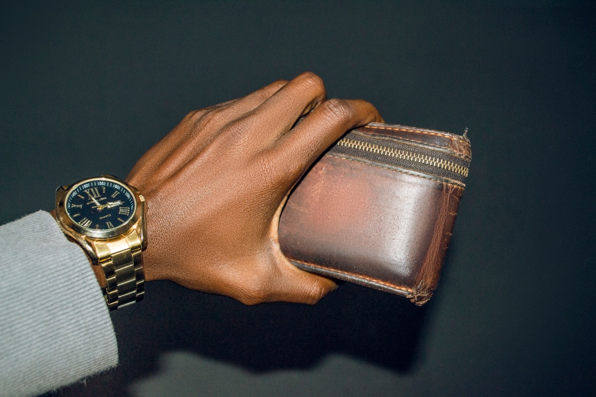 Montre-bracelet doré, portefeuille en cuir brun, main masculine.