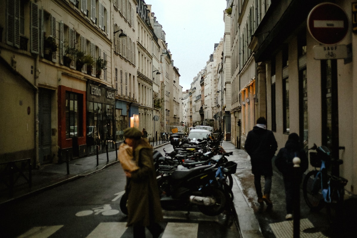 Ruelle étroite de Paris avec des piétons et des motos garées.