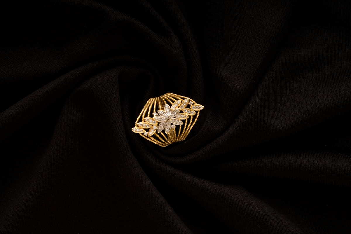 Broche dorée ornée de motifs floraux et de diamants sur fond noir.