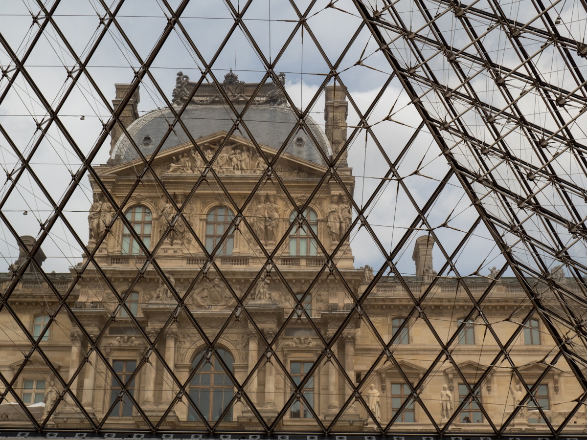 Façade ornée du Louvre à travers une structure géométrique en verre.