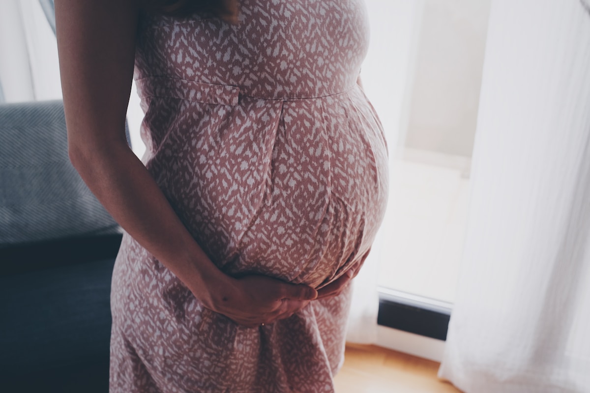Femme enceinte, robe à motifs, mains sur le ventre.