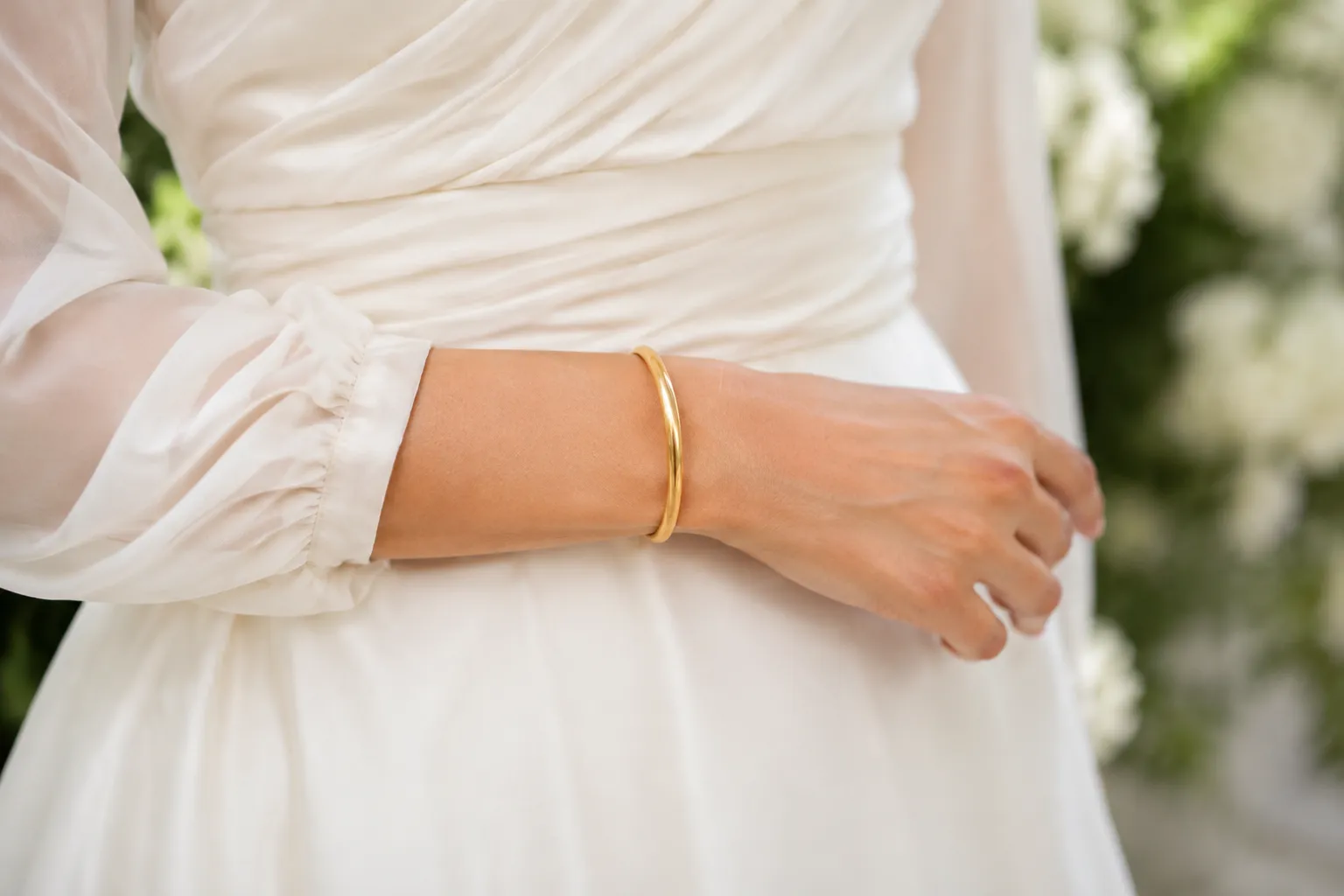 Robe de mariée blanche, bracelet doré, gros plan sur le bras.
