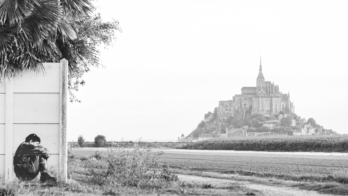 Paysage médiéval avec château sur la colline, palmier et silhouette solitaire.