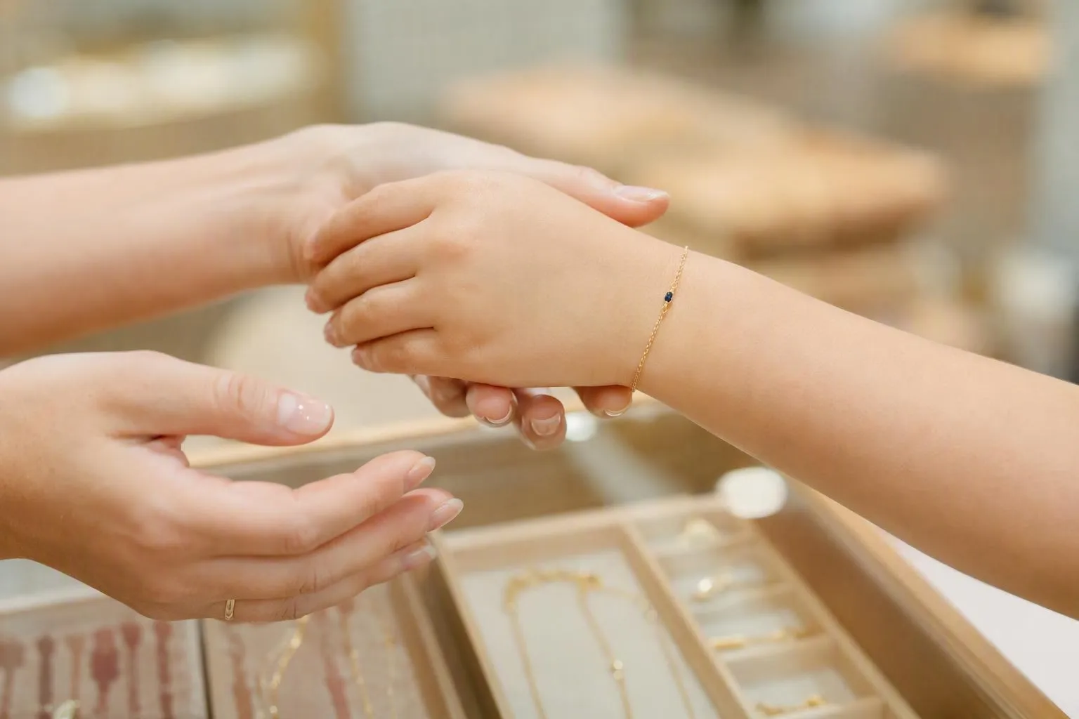 Mains féminines tenant délicatement un bracelet en or avec un petit diamant.