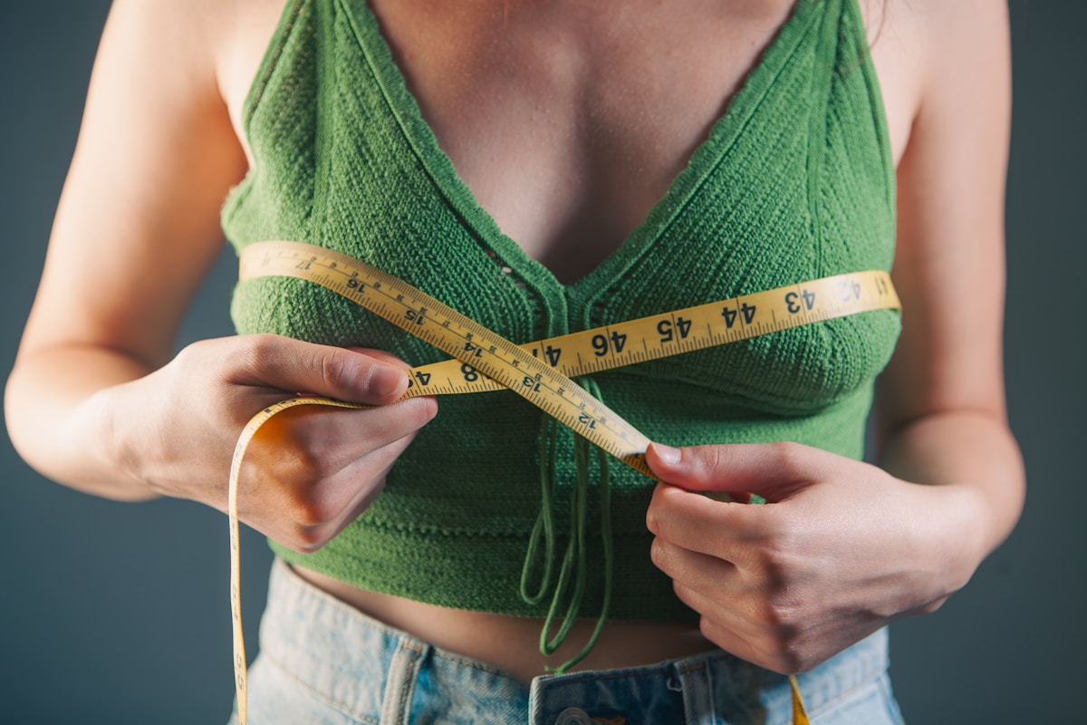 Femme en débardeur vert mesurant sa taille avec un ruban.