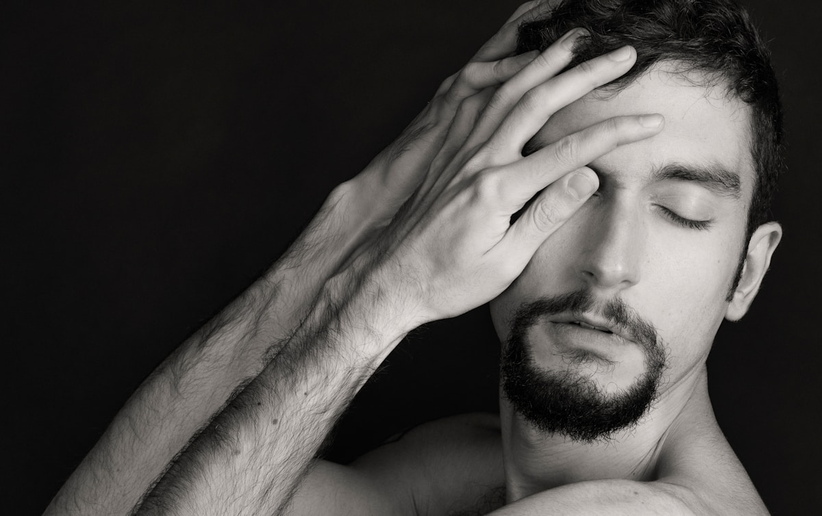Homme barbu, fatigué, le visage dans les mains, en noir et blanc.