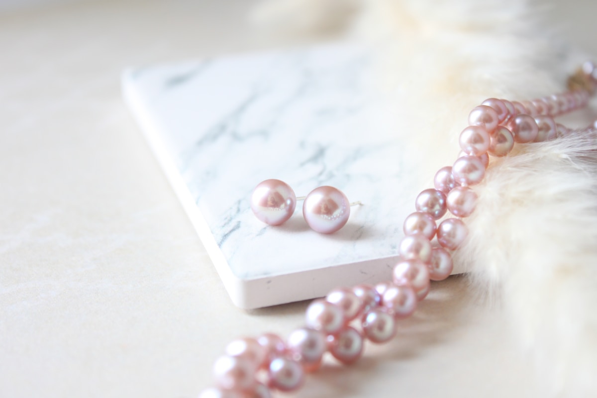 Boucles d'oreilles et collier de perles roses sur fond de marbre.