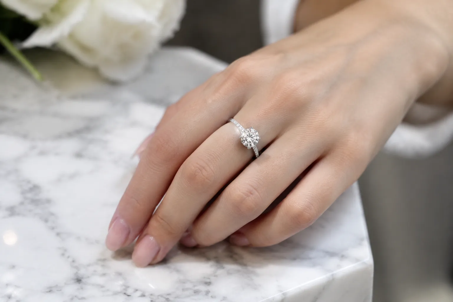 Main portant une bague de fiançailles diamant sur socle marbre, lumière douce, profondeur de champ réduite.